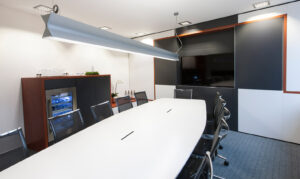 Radiox Strahlentherapie Soest, Besprechungsraum, großer Tisch mit vielen Stühlen, Getränkeschrank, Wand mit Monitor, Grau-weiß gestaltet