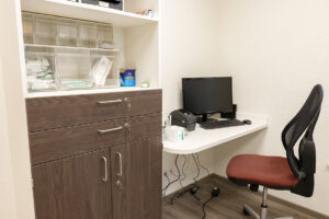 Ärztehaus Möhnesee-Körbecke, Arztzimmer mit Schreibtisch und braun-weißem Schrank mit Medikamenten