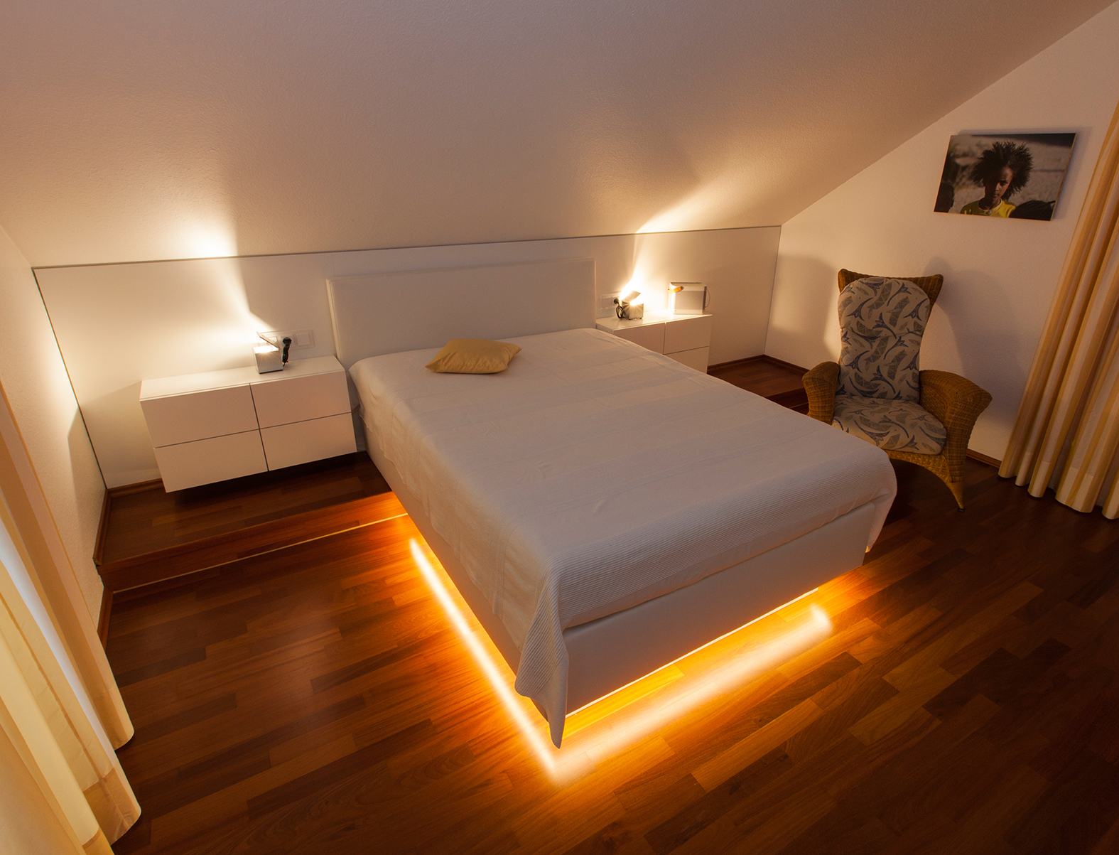 Wohnraum, Doppelbett mit Akzentbeleuchtung in Gelb, Nachtschränken und Stuhl.